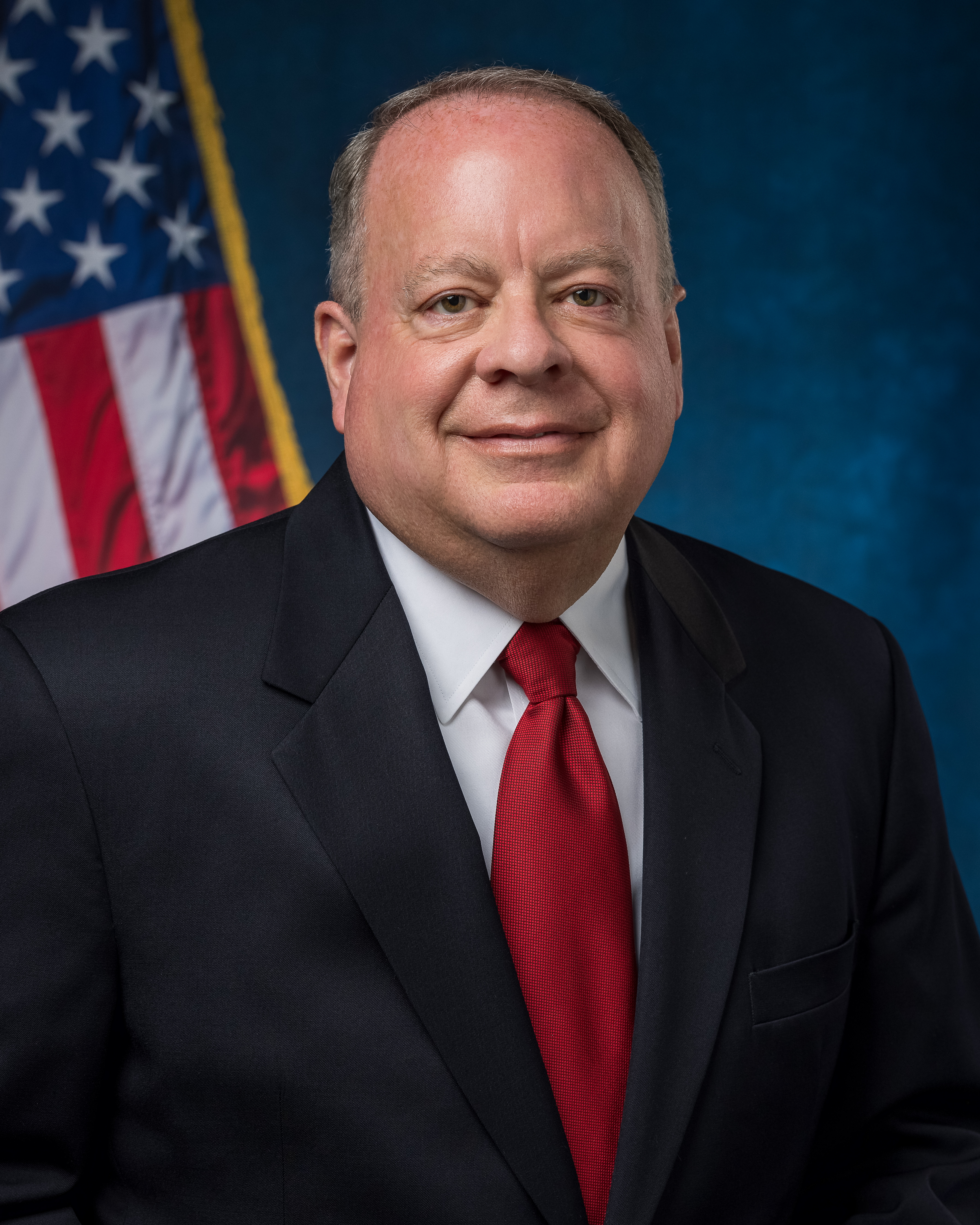Councilor Brian Whitlock in front of blue background and U.S. flag.